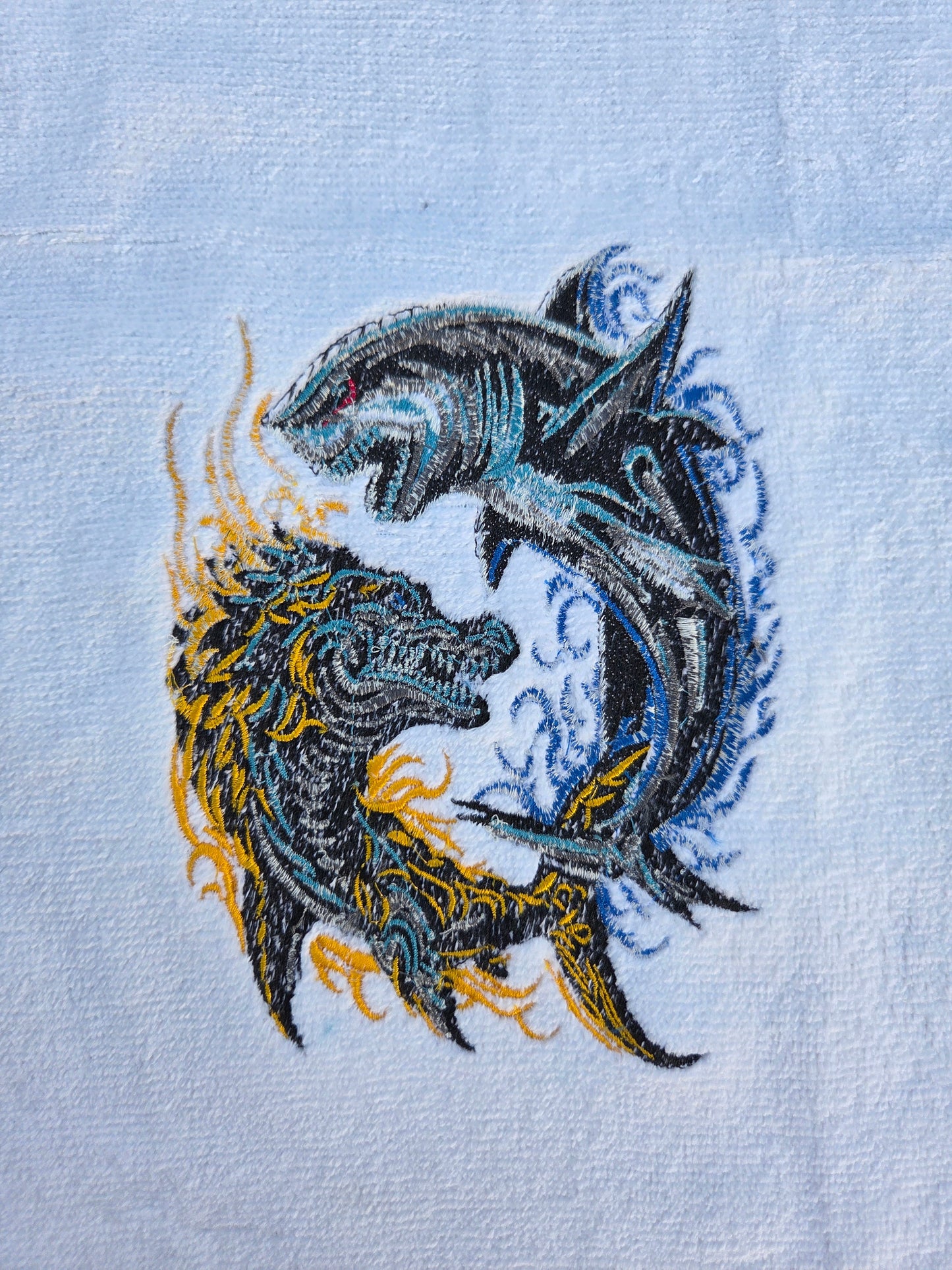 Embroidered design of two dragons on a light blue fabric background