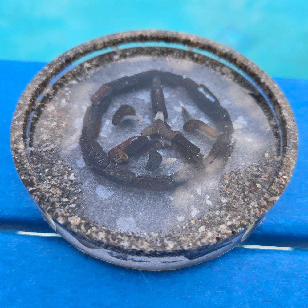 Resin coaster with fossil shark teeth forming a peace sign