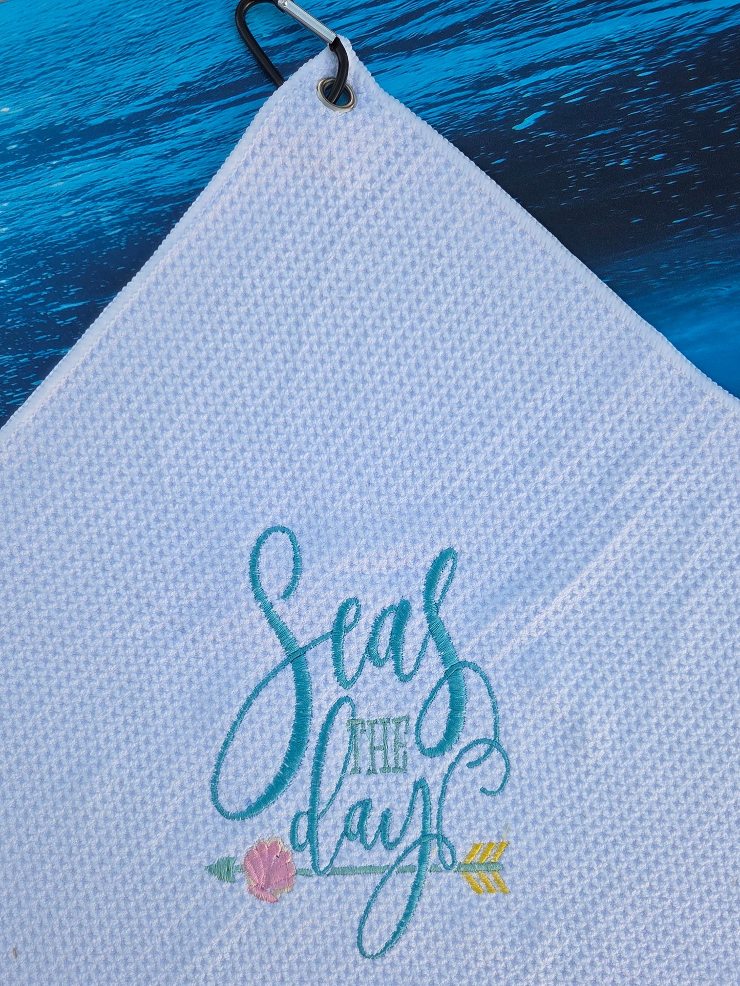 White towel with embroidered text and floral design on a blue surface