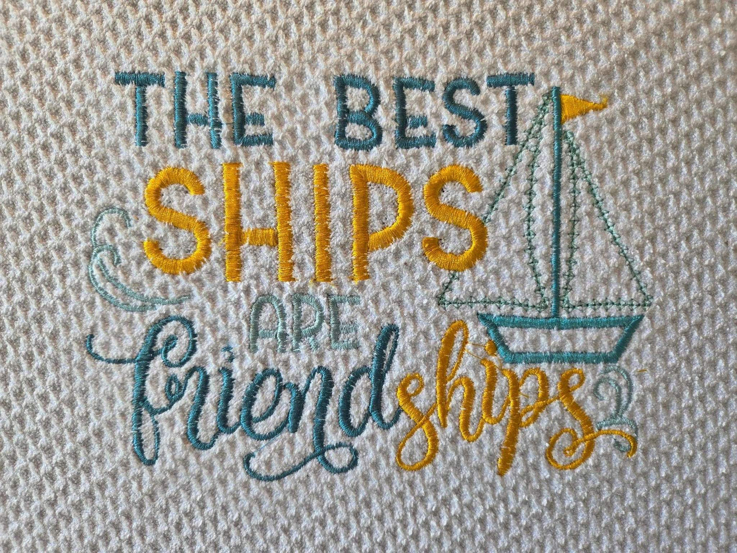 Embroidery design with 'The best ships are friendships' text and a sailboat on a textured fabric background.