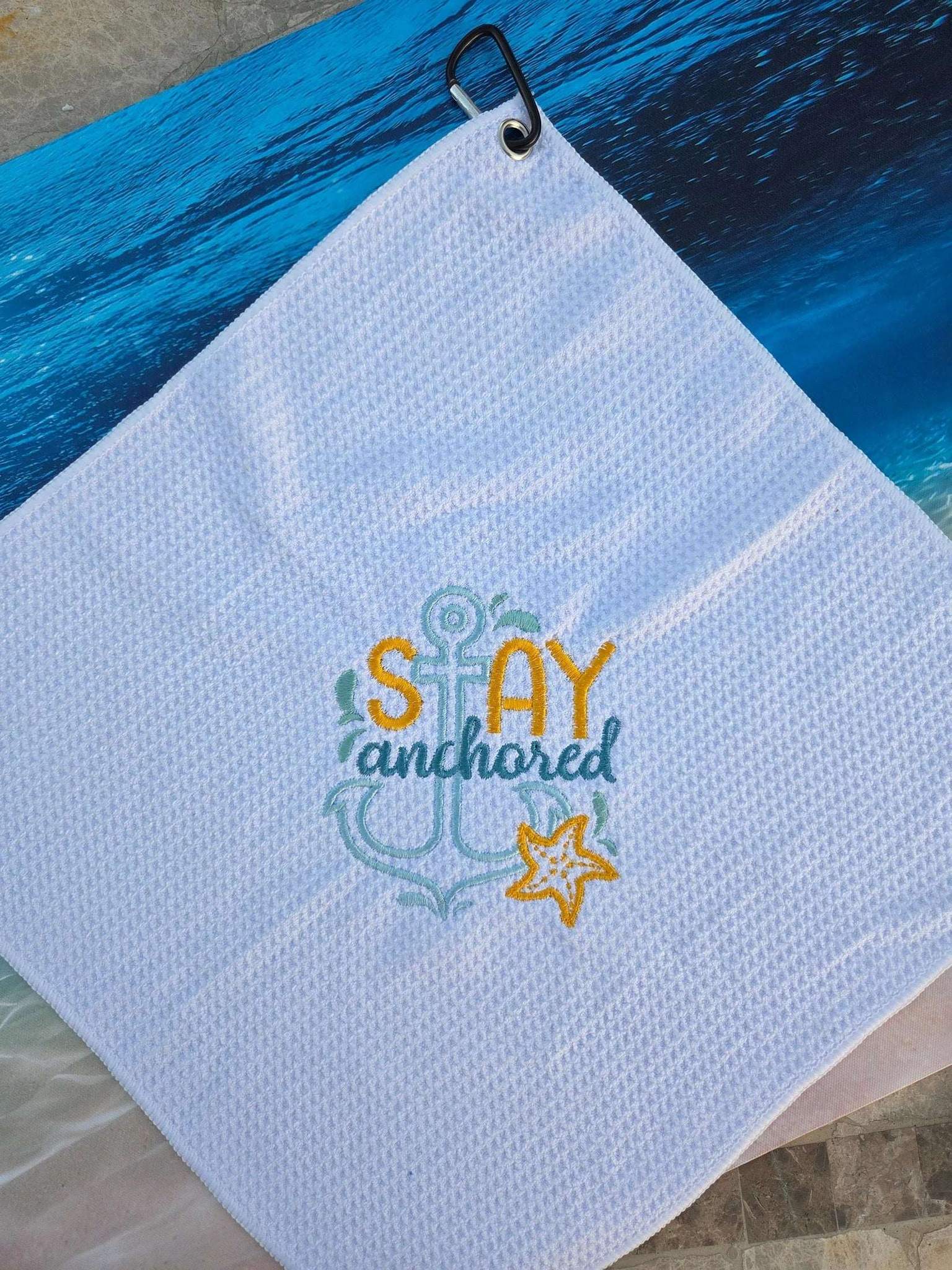 Light blue towel with 'Stay Anchored' embroidery on a blue surface