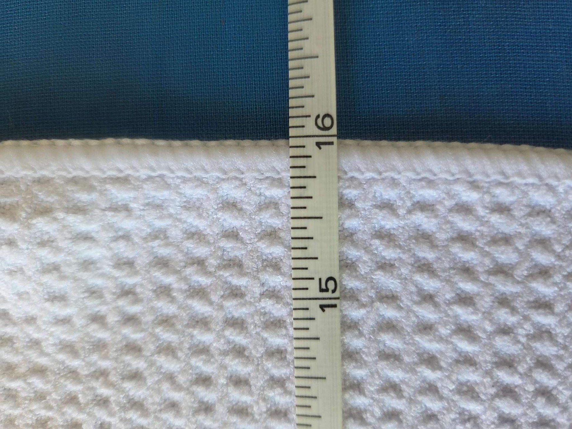 Measurement of fabric thickness with a ruler on a blue and beige textured fabric background