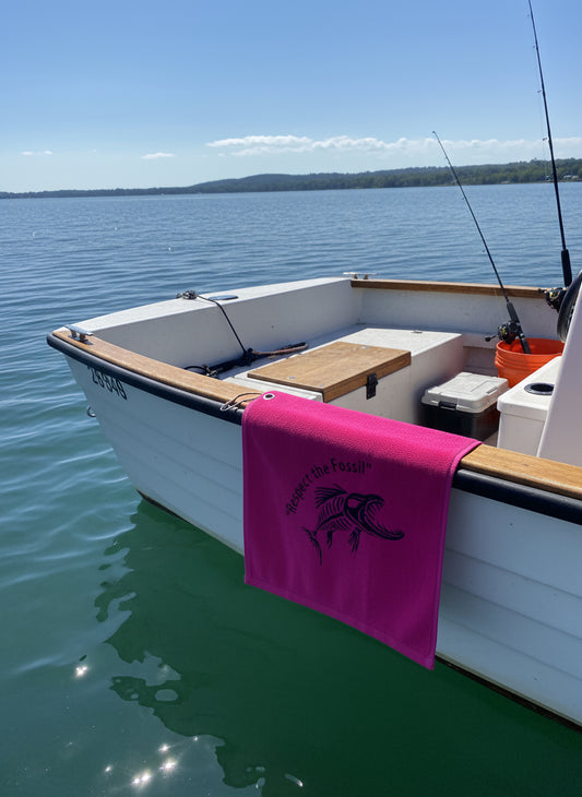 Small white boat on calm water with a pink towel draped over the side.