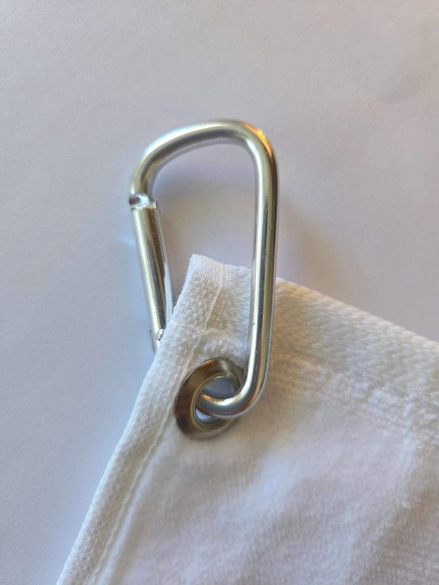 Metal carabiner attached to a white fabric bag on a light background