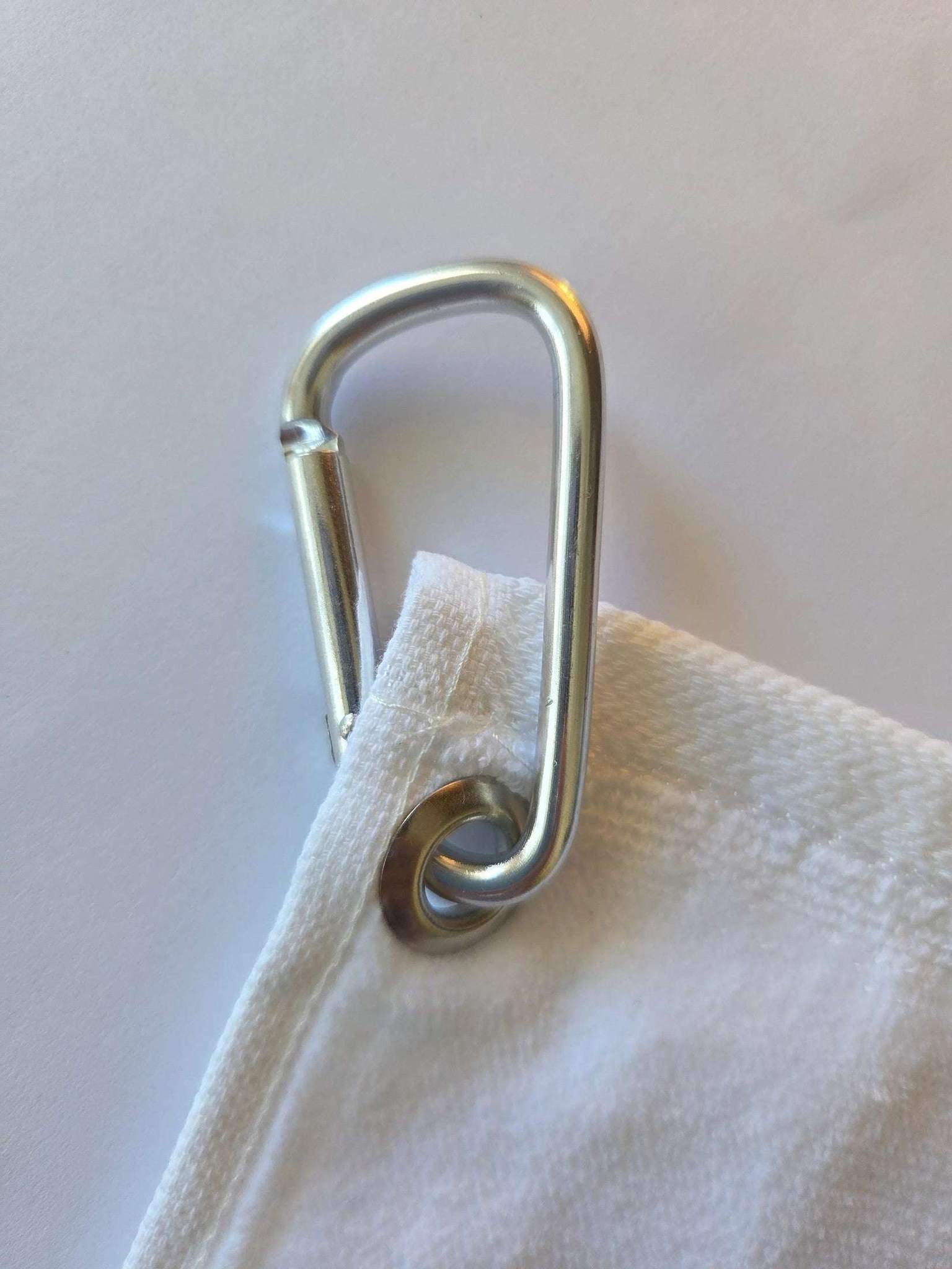 Metal carabiner attached to a white fabric bag on a light background