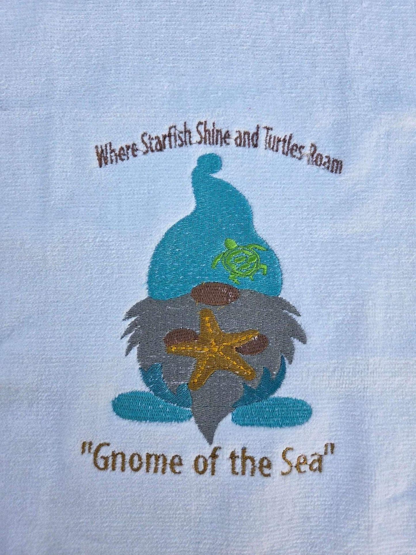 Embroidered design of a sea gnome with starfish and turtle on a light blue background.