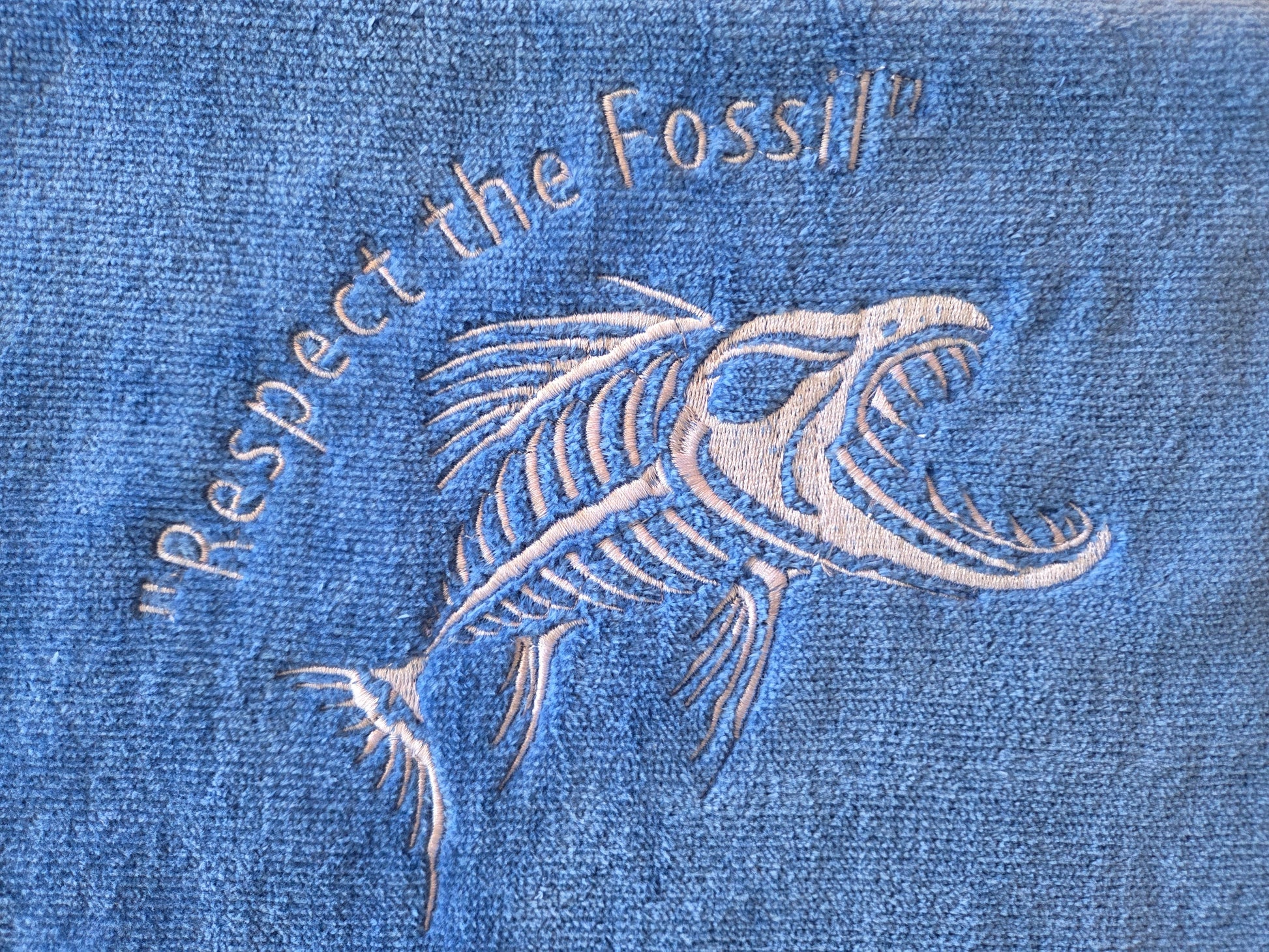 Blue denim fabric with white embroidered fish skeleton and text 'Respect the Fossil'.